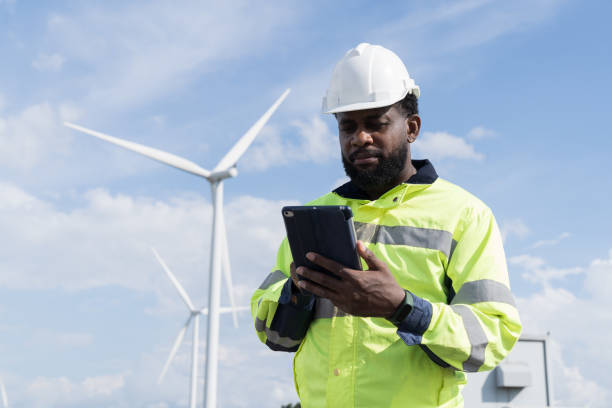 istock African American male engineer using digital tablet checking system of wind turbine at windmill field farm station. Male engineer monitoring and control windmill system at wind turbines station 2189038614