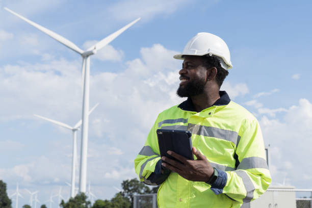 istock African American male engineer using digital tablet checking system of wind turbine at windmill field farm station. Male engineer monitoring and control windmill system at wind turbines station 2189038622