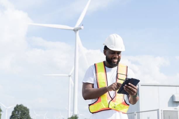 istock African American male engineer using digital tablet checking system of wind turbine at windmill field farm station. Male engineer monitoring and control windmill system at wind turbines station 2189038628