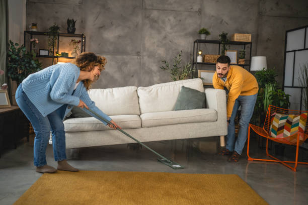 istock couple do chores clean floor with a broom under the raised sofa 2189043108