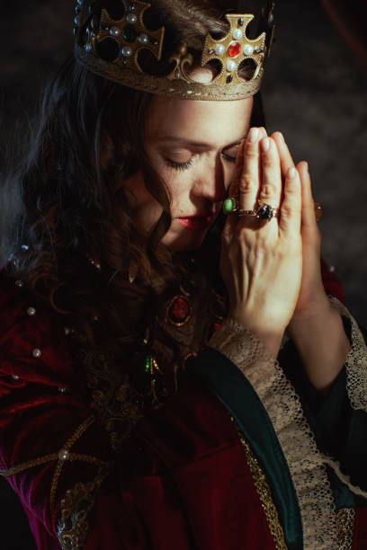 istock medieval queen in red dress with crown praying 2189045609