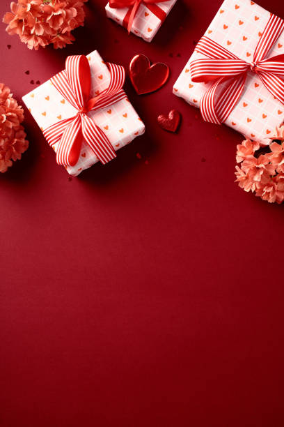 istock Valentine's Day gift boxes with heart-patterned paper and red ribbons, surrounded by red flowers and heart-shaped decorations on red vertical background. 2189049415