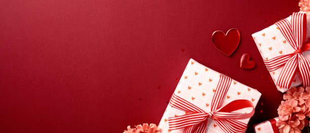 istock Valentine's Day banner with two gift boxes wrapped in heart-patterned paper and red striped ribbons, surrounded by pink flowers and heart-shaped decorations on a red background. Perfect for romantic c 2189049479