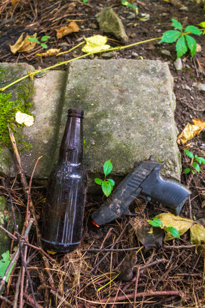istock Discarded Beer Bottle and Toy Gun on Soil Surface 2189050417