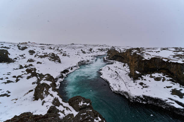 Turquoise river flowing through a snow covered canyon in the icelandic countryside during winter