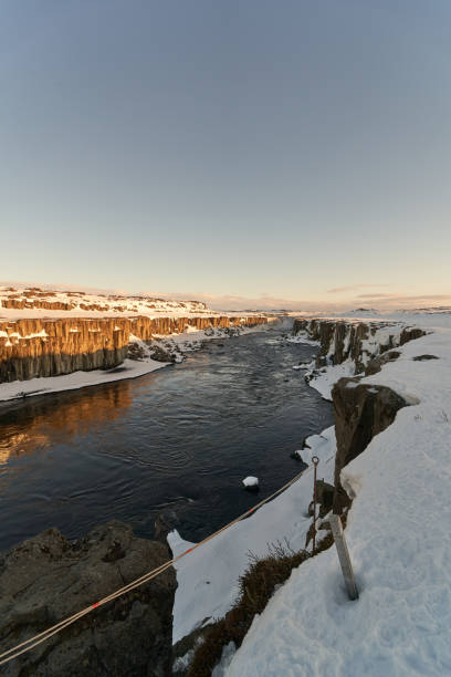 Wide river is flowing through a canyon covered in snow with the sunset reflecting on the water