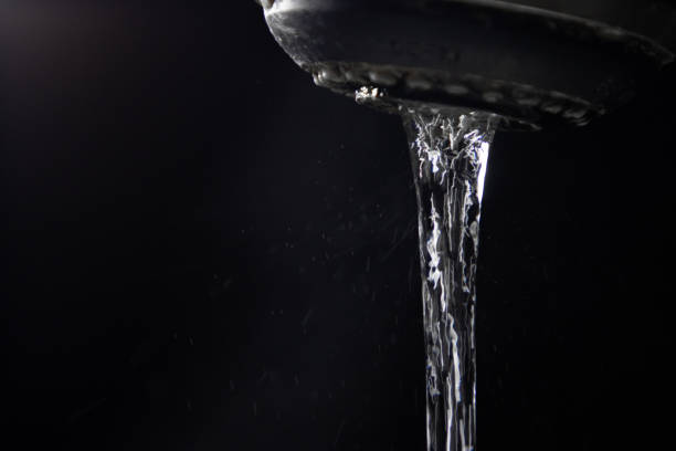 A stream of drinking water flowing from a faucet against a black background.