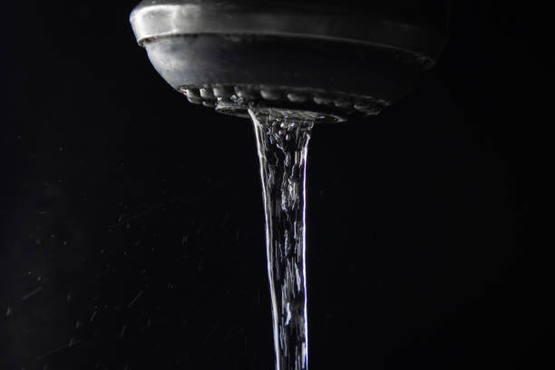A stream of drinking water flowing from a faucet against a black background.