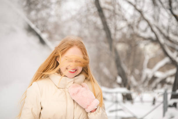 A blonde woman in a cozy beige winter jacket with pink wool gloves. Warm clothes for cold snowy weather, stylish outerwear.