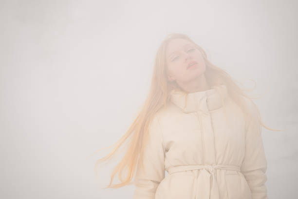 A blonde woman in a cozy beige winter jacket with pink wool gloves. Warm clothes for cold snowy weather, stylish outerwear.