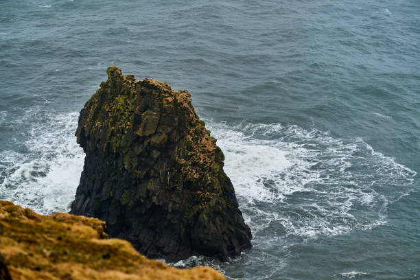 Waves are crashing against a lone sea stack rising from the ocean on a dramatic day