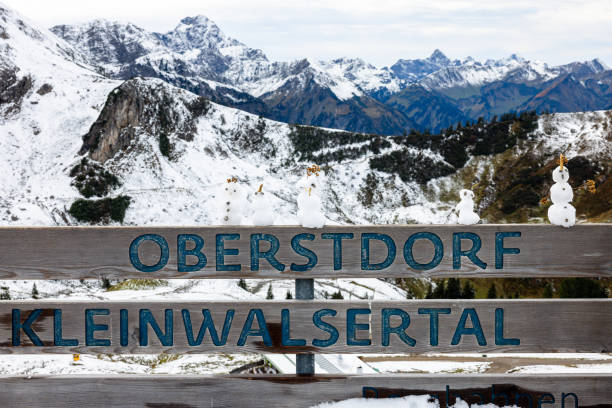 Oberstdorf Kleinwalsertal Sign on a public bench with tiny snowmen standing on top of it with the Austrian Alps covered with snow in the background