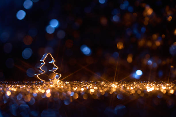 Christmas tree-shaped cookie cutter on sparkling golden lights background, with festive blue bokeh accents.