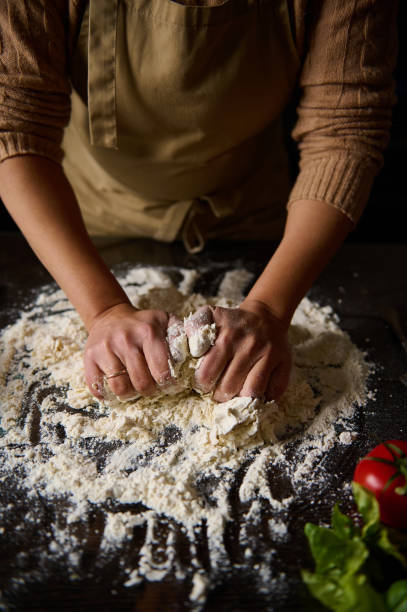 Person kneads dough on a floured surface with fresh ingredients nearby