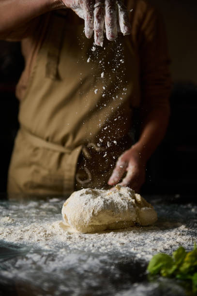 istock Close-up of baker sprinkling flour over fresh dough in kitchen setting 2189059072