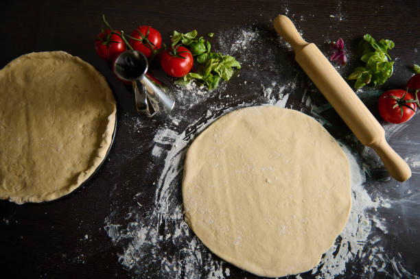 istock Fresh pizza dough with tomatoes, basil, and rolling pin on dark surface 2189059577