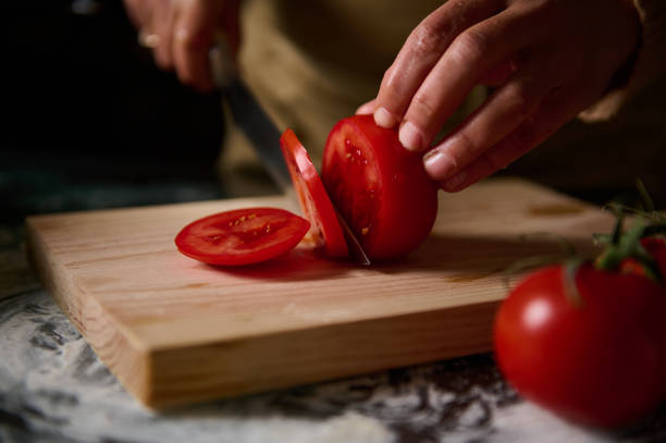 Close-up of hands slicing juicy red tomatoes on a wooden cutting board, capturing a moment in food preparation.