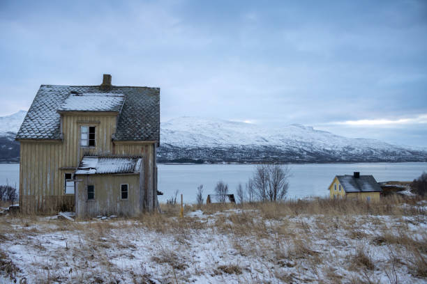 Yellow wooden abandoned house on the coast of the Norwegian sea. Mountains in the background. Land covered by snow in the late autumn. Kongsvika, Norway.