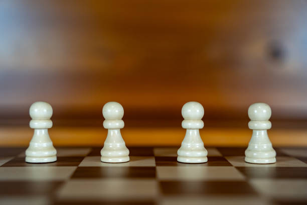 Close-up of cream pawn chess pieces on chessboard against black background.
