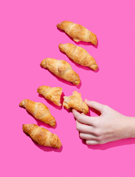 istock Hand holding fresh torn mini croissant on pink background with shadow. Design flat lay concept 2189079791