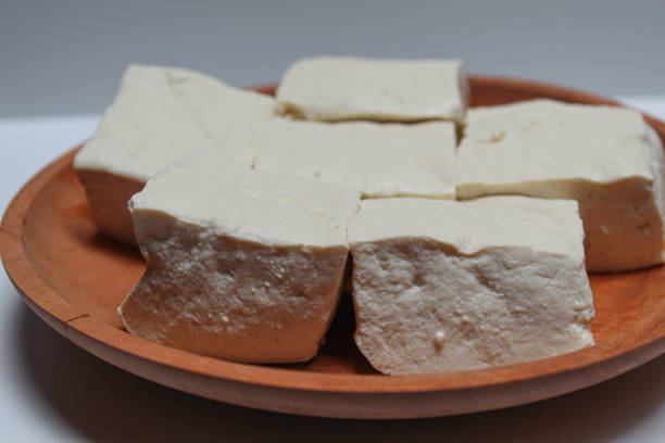 istock Uncooked white tofu on a wooden plate, isolated on white background 2189085404