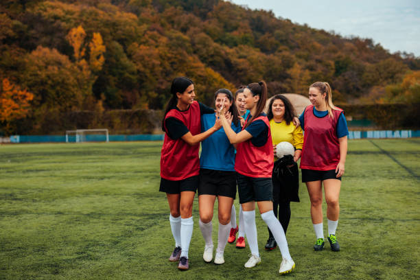 A cheerful team of female soccer players high fiving after a successful practice at the pitch.