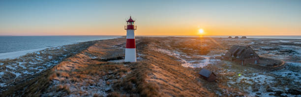 Red and white striped lighthouse situated on a coastal landscape at sunrise in winter. Lighthouse West-List on the Ellenbogen (the \
