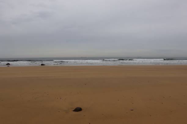 istock Wide sandy beach meeting wavy ocean under cloudy sky 2189094296