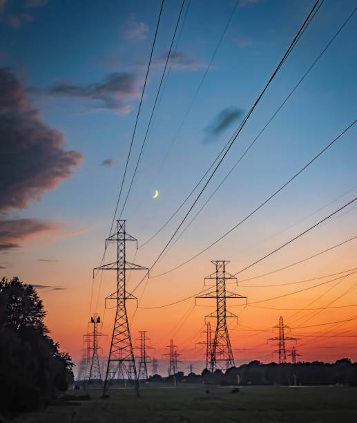 Scenic view of high-voltage power lines silhouetted against a colourful sunset sky with a crescent moon, atmospheric image captures the intersection of nature and technology in a tranquil rural setting