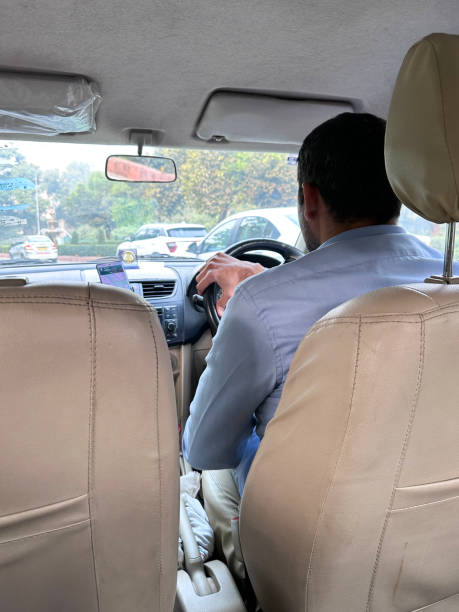 Image of Indian man driving private taxi using sat nav (satellite navigation) on Smartphone on mount, motorway viewed from cab car interior through windscreen, rear view, focus on foreground