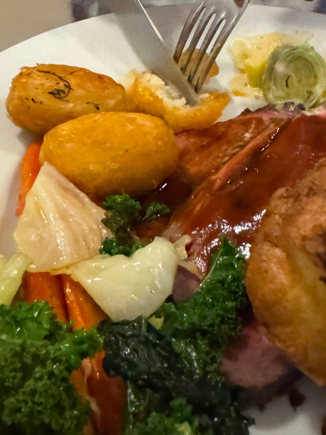 istock Full frame image of white plate containing Sunday roast dinner meal, Yorkshire pudding, carrots, roasted potatoes, cabbage, creamed leeks, slices of beef, covered in gravy, knife and fork cutting potato, elevated view, focus on foreground 2189124237