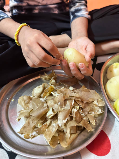 istock Full frame image of unrecognisable girl sat cross-legged on floor, preparing dinner, peeling cooked boiled potatoes by hand, placing skins onto stainless steel thali plate, focus on foreground 2189124658