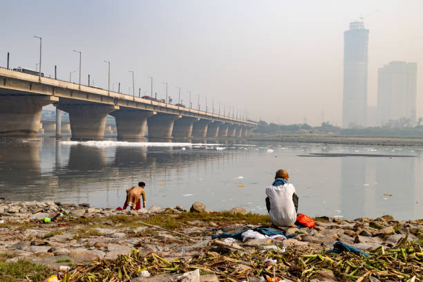 istock devotee performing holy rituals at Polluted River shore with Toxic Foam and misty city view 2189125650