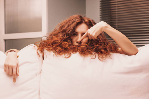 istock Young woman with red hair lying on sofa making funny faces 2189126313