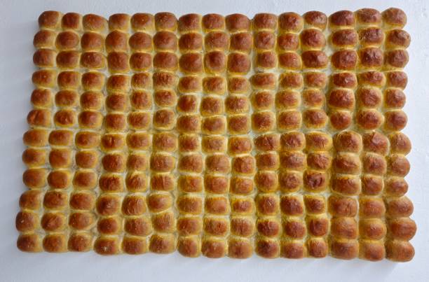 Rows of bread-like or bun-like objects arranged neatly. They appear golden-brown, likely freshly baked.Pav is a soft, slightly sweet, square-shaped bread roll that is a staple in Indian cuisine
