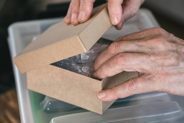 istock Elderly female hands getting the package out of small cardboard box, close-up, selective focus. 2189131693