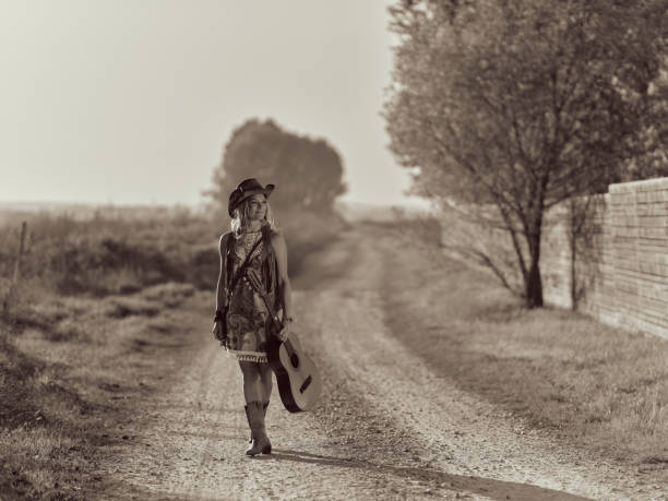 Black and white photography of carefree country musician enjoying while walking with a guitar on dirt road in nature. Copy space. Photographed in medium format.