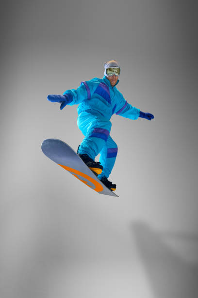 istock Athletic snowboarder balancing gracefully in mid-air jump, dressed vibrant blue jumpsuit against grey studio background. Excitement of snowboarding. 2189147637