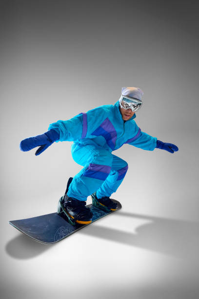 istock Snowboarder in striking winter gear, against grey studio background, performing tricks that embody thrill of extreme sports and adventure. 2189147641