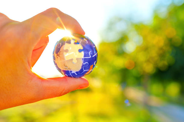 istock Hand Holding Globe Puzzle Piece with Sunlight and Nature Background 2189147917