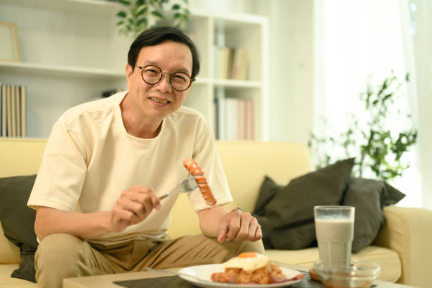 istock Happy middle aged man sitting on sofa, enjoying a plate of fried rice 2189150083