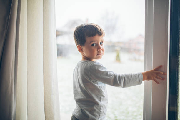 istock Little boy looking outside through the window, bad weather, quarantine 2189150276