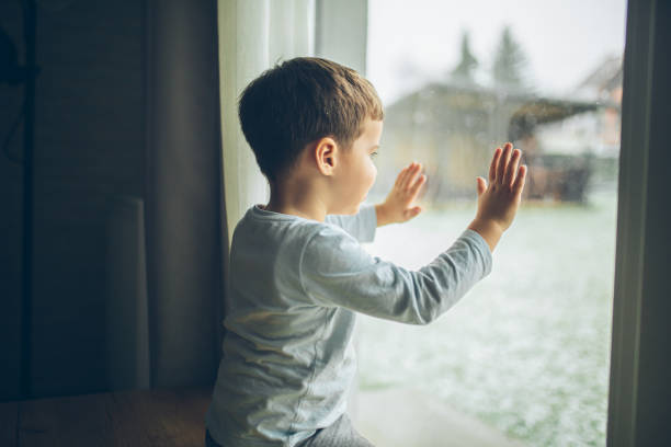 istock Little boy looking outside through the window, bad weather, quarantine 2189150356