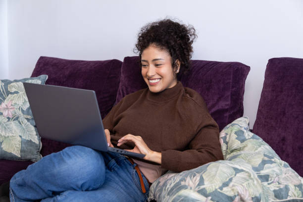 istock Young woman working remotely from home on laptop, smiling and relaxing on sofa 2189150363