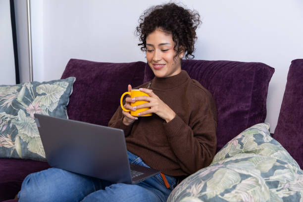 istock Young woman relaxing on sofa with laptop and coffee 2189150373
