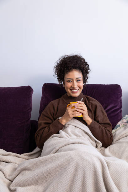 istock Young woman relaxing on sofa with warm drink, smiling at camera 2189150378