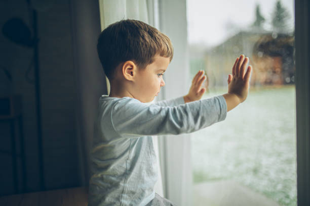 istock Little boy looking outside through the window, bad weather, quarantine 2189150414