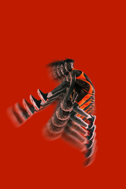 Basketball player mid-air holding ball, bold red background. Stroboscopic effect enhances dynamic phases of jump, focusing on strength and action.