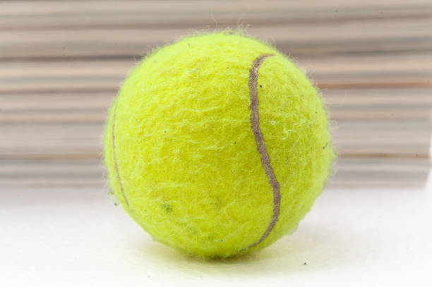 A tennis ball is sitting on a white surface. The ball is yellow and fuzzy