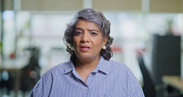 istock Indian serious old aged business woman lady sitting look camera do work distant conversation client on video call indoor office. Head shot portrait elder adult expert female worker staff speak conference at job place 2189152898